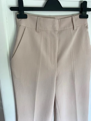 Kostymbyxor - Na-Kd - Beigea kostymbyxor från NAKD. Storlek 32. Endast använda ett fåtal gånger. I mycket fint skick 🌸 Längd - ca 92cm (innerbenslängd ca 65cm).