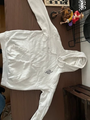 Vit hoodie med ormtryck från YOURTURN - Säljer en vit hoodie från YOURTURN med en snygg orm broderad på bröstet. Hoodien har klassisk känguruficka, dragsko i huvan och är gjord i mjukt bomullsmaterial. Perfekt för dig som gillar stilrena plagg med en twist.