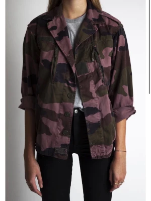 Camouflage jacka i bomull - Snygg camouflage jacka i grönt, svart och lila-rosa toner. Jackan har klassisk krage, knäppning framtill och två bröstfickor med dragkedja. Tillverkad i bomull och har långa ärmar som kan vikas upp för en avslappnad look. Nypris 2 500 kr. I mycket bra skick, använt fåtal gånger!