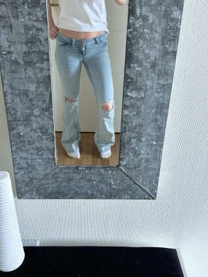 Ljusblå Lågmidjade bootcut jeans med hål - Jag säljer mina ljusblåa Lågmidjade bootcut jeans från nelly med hål vid båda knäna och rosa detaljer på fickorna. Dom är nästintill helt nya och oanvända då dom tyvärr inte passar☺️