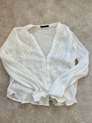 Vit blus med broderi från Zara - Superfin vit blus från Zara med broderade detaljer framtill och knappar längs hela framsidan. Använd en gång har krympt lite i första tvätten så används inte. Den är i str M men skulle säga passar som S nu 