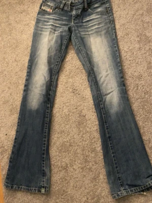 Blå bootcut jeans från diesel  - Snygga blå bootcut jeans från diesel med slitningar och ljusa partier framtill och baktill. Klassisk femficksmodell med låg midja och dragkedja. Perfekta för en avslappnad och trendig look.