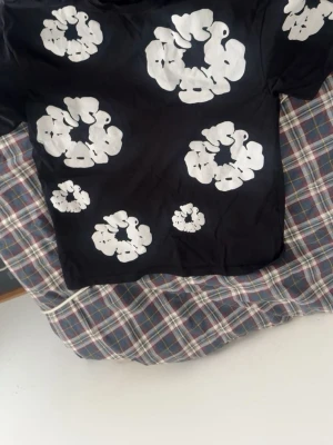 Svart t-shirt med vita blommor - Cool svart t-shirt med stora vita blommor tryckta över hela framsidan. T-shirten har en klassisk passform och korta ärmar. Perfekt för dig som vill sticka ut med ett unikt mönster. Materialet känns mjukt och bekvämt mot huden. Pris kan diskuteras vid snabb affär!