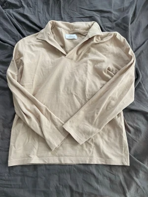 Beige långärmad tröja från Ciszere - Säljer en beige långärmad tröja från Ciszere med krage och v-ringning. Tröjan är tillverkad i ett mjukt, tunt tyg och har en avslappnad passform. Perfekt för en chill och stilren look.