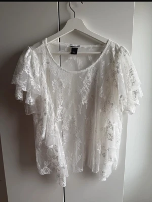 Vit spetsblus med volangdetaljer - Superfin vit blus i transparent spets med korta ärmar och volangdetaljer längs sidorna. Perfekt för dig som gillar romantisk och luftig stil. Blusen har rund halsringning och är lätt croppad. Slutsåld💕