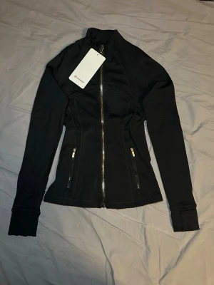 Lululemon define jacket guld svart - Helt ny oanvänd Lululemon kofta perfekt för träning. Säljs oanvänd med tags som sitter på samt kvitto. Storlek 2