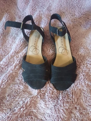 Svarta sandaler från Din Sko - Snygga svarta sandaler från Din Sko med öppen tå och justerbart spänne runt ankeln. Skorna har en klassisk design med korslagda remmar framtill och en liten klack. Perfekta för varma dagar och passar till många olika outfits.