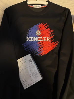 Svart Moncler sweatshirt med tryck - Cool svart sweatshirt från Moncler med stort broderat Moncler-tryck i blått och rött framtill. Snygg moncler design på ryggen. Rund halsringning och långa ärmar. Kommer med signatur, kvitton, moncler kort, pris kan diskuteras 🙏