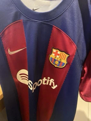 FC Barcelona matchtröja Nike - Säljer en officiell FC Barcelona matchtröja från Nike med klassiska blå och vinröda ränder. Tröjan har klubbmärke, Nike-logga och Spotify som sponsor framtill. Tillverkad i lätt och ventilerande material, perfekt för fotbollsträning eller match.