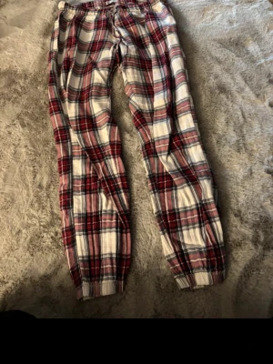 Rutiga pyjamasbyxor i rött och vitt - Mysiga pyjamasbyxor med klassiskt rutmönster i rött, vitt och svart. Byxorna har resår i midjan och vid bensluten för extra komfort. Perfekta för chillkvällar hemma. Materialet känns mjukt och skönt mot huden.