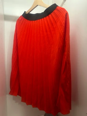 Röd plisserad kjol från loul Edition - Snygg röd plisserad långkjol från Xoul Edition med bred svart midjeresår. Kjolen har ett stilrent uttryck och passar perfekt för dig som vill sticka ut med färg. Materialet känns lätt och flowy.