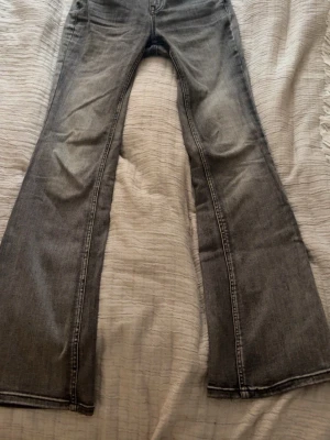 Grå bootcut jeans med slitningar - Säljer ett par grå bootcut jeans med lätt slitna detaljer och klassisk femficksmodell. Jeansen har utsvängda ben.