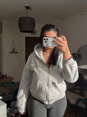 Ljusgrå zip hoodie med huva - Säljer en ljusgrå hoodie med dragkedja och huva. Hoodien har ribbade muddar vid ärmslut och nederkant samt en klassisk, avslappnad passform. Perfekt för chill dagar eller när du vill ha något bekvämt. Materialet känns mjukt och skönt mot huden.
