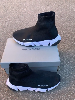 Balenciaga Speed Trainer svarta sneakers - Säljer ett par svarta Balenciaga Speed Trainer sneakers med vit chunky sula och stickad ovandel. Skorna har en strumpliknande passform och Balenciaga-logga på sidan. Perfekta för dig som gillar streetwear och vill ha något bekvämt och stilrent.