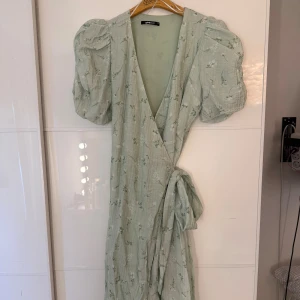 Grön blommig omolottklänning - Säljer denna omlottklänning från Gina tricot i strl 34 som använts vid få tillfällen. Perfekt till till sommaren och lite finare tillställningar.