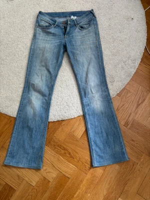 Blå bootcut jeans med låg midja - Säljer ett par ljusblå bootcut jeans från Lee med klassisk femficksmodell och slitna detaljer. Jeansen har normal midja och dragkedja med knapp. 