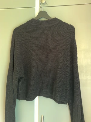 Svart stickad tröja från H&M Divided - En svart stickad tröja från H&M Divided med avslappnad passform och ribbad rund hals. Tröjan har långa ärmar och är gjord i ett mjukt, tjockare material som passar perfekt för kyligare dagar. Enkel och stilren design som är lätt att matcha.