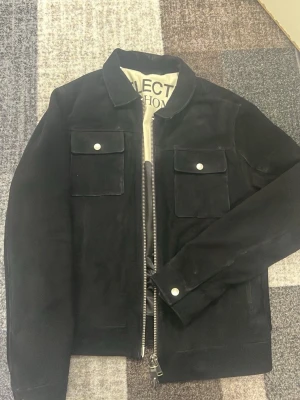 Svart mockajacka från Selected Homme - Stilren svart mockajacka från Selected Homme med två bröstfickor med lock och silverfärgade knappar. Jackan har dragkedja framtill och en mjuk, svart innerfodring. Perfekt för dig som vill ha en klassisk och trendig look.