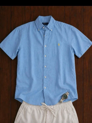 Ralph Lauren Skjorta Herr Small Ljusblå  - Snygg och klassisk kortärmad Polo Ralph Lauren-skjorta i ljusblå färg. Perfekt till sommaren, semester, student, middagar eller en avslappnad preppy-look. Broderad Ralph Lauren-logga på bröstet. Mycket lättmatchad med vita shorts, chinos eller jeans.                                                   Kommer från ett rökfritt hem.                                 Snabb leverans. 📦                                             Bundeldeals finns  