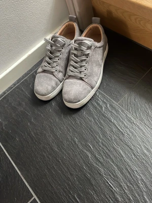 Christian Louboutin skor - Knappt använda Snygga gråa sneakers från Christian Louboutin med klassisk röd sula och diskret logga undertill. Skorna har en låg profil, rund tå och är tillverkade i mocka med vita gummisulor. Perfekta för dig som vill sticka ut med exklusiva detaljer. 