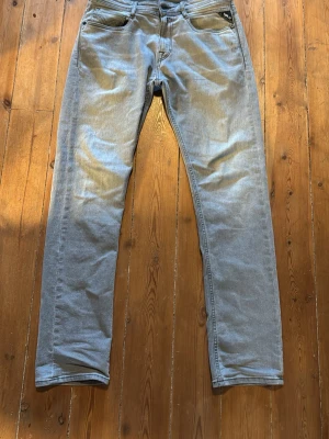 Ljusgrå raka jeans från Replay - Snygga ljusgrå jeans från Replay med rak passform och klassiska fem fickor. Jeansen har diskreta sömmar och en stilren look, perfekta för en avslappnad stil. Materialet är mjukt denim som ger en bekväm känsla hela dagen.