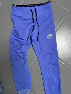 Lila Nike Air mjukisbyxor - Säljer ett par lila Nike Air mjukisbyxor med svart dragsko i midjan och logga på vänster lår. Byxorna har smal passform, ribbade muddar vid benslut och meshpaneler på benen för extra ventilation. Perfekta för chill eller träning.