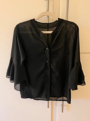 Svart blus med volangärm - Svart blus med tajta ärmar med volang längst ner. Inget märke eller storlek men skulle gissa på xs/s