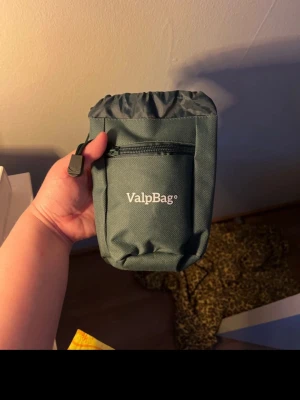 Grön ValpBag för hundgodis - Smidig grön ValpBag i slitstark textil med dragkedjeficka framtill och snörstängning upptill. Perfekt att ha hundgodis eller småprylar i när du är ute med hunden. Fästes enkelt med en svart rem på baksidan.