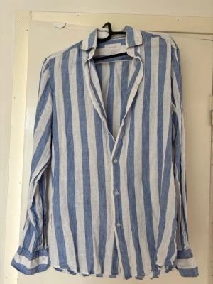 Blåvit randig linneskjorta Massimo Dutti - Snygg blåvit randig skjorta från Massimo Dutti i 100% linne. Skjortan har klassisk krage, knäppning framtill och långa ärmar. Perfekt för en avslappnad och stilren look.