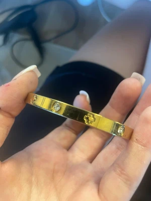 Guldigt armband med stenar - Snyggt armband i guldfärgad metall med blanka ytor. Armbandet har infällda klara stenar och små dekorativa blommönster runt om. Perfekt accessoar för dig som gillar stilrena och eleganta detaljer.köpt i Montenegro och den rostar inte