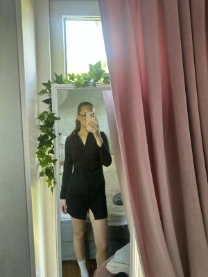 Svart kort klänning med slits - Säljer en svart kort klänning med v-ringning och lång ärm. Klänningen har en snygg slits framtill och markerad midja för en smickrande siluett. Perfekt för dig som gillar stilrena och trendiga plagg.