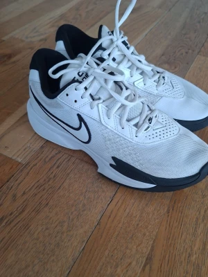 Nike G.T. Cut Academy vita sneakers - Snygga vita Nike G.T. Cut Academy sneakers med svart swoosh och detaljer. Ovandelen är i mesh och syntet för bra andningsförmåga och komfort. Klassisk låg modell med vita skosnören och svart vadderad häl. Perfekta för dig som gillar sportig stil.