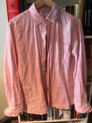Rosa linneskjorta från Uniqlo - Säljer en ljusrosa skjorta från Uniqlo i mjukt linne. Skjortan har klassisk krage, knäppning framtill, bröstficka och långa ärmar. Perfekt för en avslappnad och stilren look. Den sitter något mindre än Medium skulle jag säga.