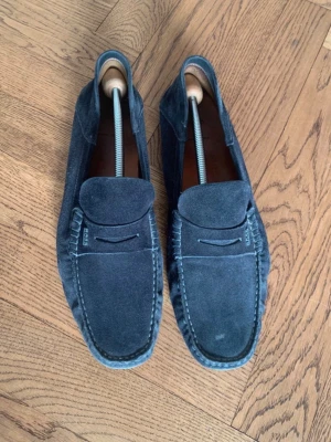 Mörkblå Hugo boss loafers  - Snygga mörkblå loafers i mocka från Hugo med klassisk båtskor design och diskret logga på sidan. Storlek 43. Perfekta för sommaren nu och passar utmärkt att ha uppklätt till ett par chinos eller linnebyxor. Fungerar även i vardagen fint. Nypris ligger på 2399, släpper till bra pris. Pris är diskuterbart vid en snabb och enkel affär. OBS INGA SKAMBUD❌ Vid fler frågor eller funderingar är det bara att höra av sig!
