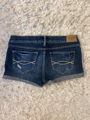 Blå jeansshorts från Abercrombie & Fitch - Mörkblå jeansshorts från Abercrombie&fitch. Storlek w27, midjemåttet är 38cm rakt över. Skriv för fler bilder! Hör av er vid några funderingar!