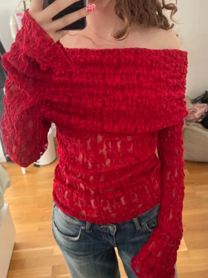 Röd offshoulder mesh topp - Använd en gång. Trendig röd offshoulder topp i mesh med transparent struktur och långa ärmar. Toppen har en croppad känsla och är stretchig med snygg textur. Perfekt för dig som vill sticka ut och älskar statement-plagg.