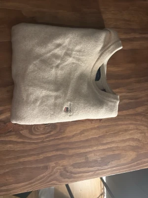 Beige stickad tröja från GANT - Tröjan är storlek L men passar xs- m perfekt Snygg beige stickad tröja från GANT med rund halsringning och ribbade muddar. Tröjan har en liten broderad GANT-logga på bröstet och är gjord i mjukt material som känns lyxigt. Perfekt för dig som gillar klassisk och stilren design.
