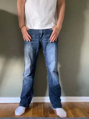 Vintage jeans - Säljer ett par vintage blå jeans med liten bootcut och snygga slitningar framtill och baktill. Jeansen har fem fickor och coola detaljer på bakfickorna. Perfekta för en avslappnad och trendig look. Materialet är denim i bomull. 