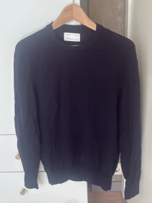 Mörkblå stickad tröja från Zara - En stilren mörkblå stickad tröja från Arket med rund halsringning och långa ärmar. Tröjan har ribbade muddar vid ärmslut och nederkant. Perfekt basplagg i garderoben och passar till det mesta. S-M i storlek.