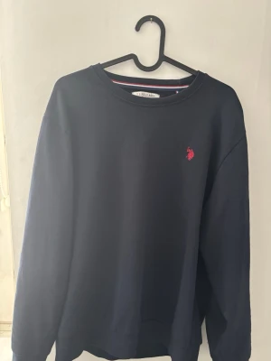 Mörkblå sweatshirt U.S. Polo Assn - Snygg mörkblå sweatshirt från U.S. Polo Assn med det klassiska röda logotrycket på bröstet. Tröjan är gjord i mjukt bommulsmaterial. Priset kan diskuteras!