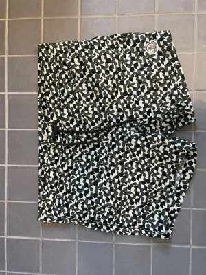 Moncler mönstrade badbyxor M - Säljer ett par snygga badbyxor från Moncler i storlek M. De har ett svartvitt geometriskt mönster, dragsko i midjan och meshfoder på insidan. Perfekta för stranden eller poolen och riktigt stilrena för dig som vill sticka ut.