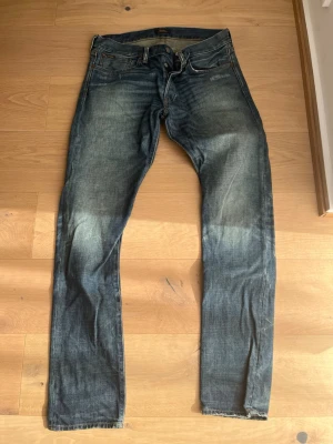 Blå smala jeans från Nudie Jeans - Säljer ett par blå smala jeans från Nudie Jeans med klassisk femficksmodell och slitningar på benen. Jeansen har en snygg tvättad look och är tillverkade i bomull. Perfekta för dig som gillar en avslappnad men stilren stil.