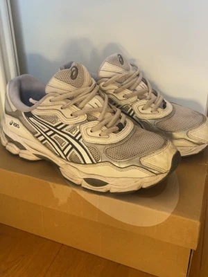 Beige ASICS sneakers med mesh och skinn - Snygga sneakers från ASICS i beige och grå toner med svarta och vita detaljer. Skorna har en chunky sula, meshpaneler för extra andningsförmåga och klassiska ASICS-loggan på sidan. Perfekta för en sportig och trendig look.