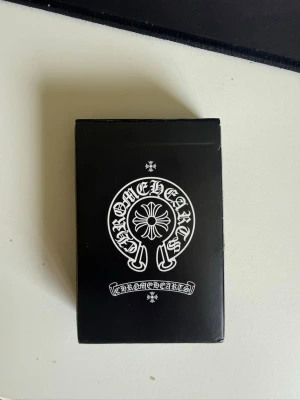 Chrome Hearts kortlek - Säljer en snygg  Chrome Hearts kortlek med svart och vit design. Kortleken har unika mönster med Chrome Hearts-logga och detaljerade blommor på baksidan. Kortens framsida har klassiska symboler i rött och svart. Perfekt för dig som gillar coola accessoarer.