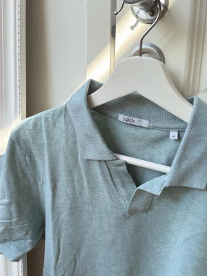 Ljusgrön piké t-shirt från Bläck strl M - Snygg pikétröja från Bläck med klassisk krage och korta ärmar. Tillverkad i mjuk bomull som känns skön mot huden. Perfekt till jeans eller shorts för en clean och enkel stil.