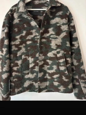 Camo overshirt från Peak Performance - Snygg overshirt från Peak Performance i camomönster med gröna, bruna och grå toner. Rak passform, klassisk krage och två stora fickor framtill. Materialet är ullmix som ger en mjuk och varm känsla. Perfekt lager på lager-plagg för kyligare dagar.