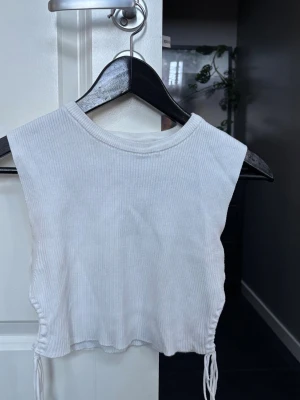 Vit ribbad crop top med snörning - Säljer en vit ribbad ärmlös crop top med rund hals och snörning på sidorna. Enkel och stilren design som är lätt att matcha. Toppen är från Zara i storlek S. 