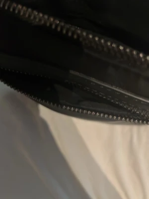 Svart valentino mesinger bag - En stilren svart valentino  mesinger bag med dragkedja och slät yta. Väskan har ett rymligt innerfack och detaljer i metall. Passar perfekt för dig som gillar minimalistisk design och enkelhet.