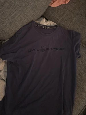 Mörkblå Sail Racing t-shirt - Snygg mörkblå t-shirt från Sail Racing med tryckt logga på bröstet. Klassisk rund hals och korta ärmar, perfekt för en avslappnad stil. Tillverkad i mjuk bomull som känns skön mot huden.
