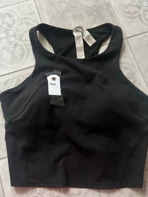 Svart croppad träningstopp Lululemon - Snygg svart croppad träningstopp från Lululemon med sportig racerback-design. Tillverkad i ett stretchigt och mjukt material som passar perfekt till träning. Enkel och stilren look som är lätt att matcha.